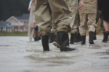 A group of people wade through a flooded street in rain boots