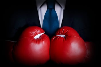 A man in a suit wears boxing gloves, prepared to fight his insurance company