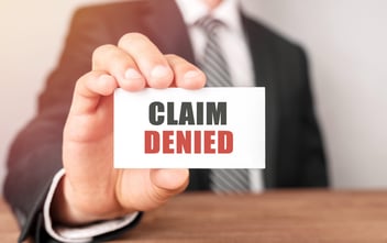 A man holds up a piece of paper, indicating that an insurance claim has been denied