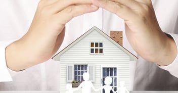 A pair of hands cup a small model home, signifying the protection of home insurance