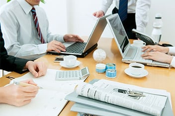 A group sits at a table with a calculator, notes, and laptops to discuss an insurance claim